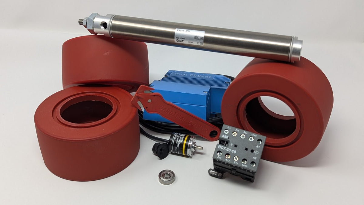 Industrial replacement parts on white: red rollers, a pneumatic cylinder, an encoder, a contactor, a bearing and a safety cutter